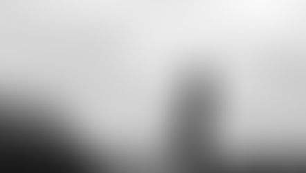 Pregnant woman in profile stands outdoors, city skyline in background. Overcast sky, serene mood, silhouette effect.
