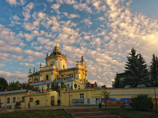 Baroque-style building under a sky with scattered clouds. Trees and a colorful mural adorn the foreground, creating a serene atmosphere.