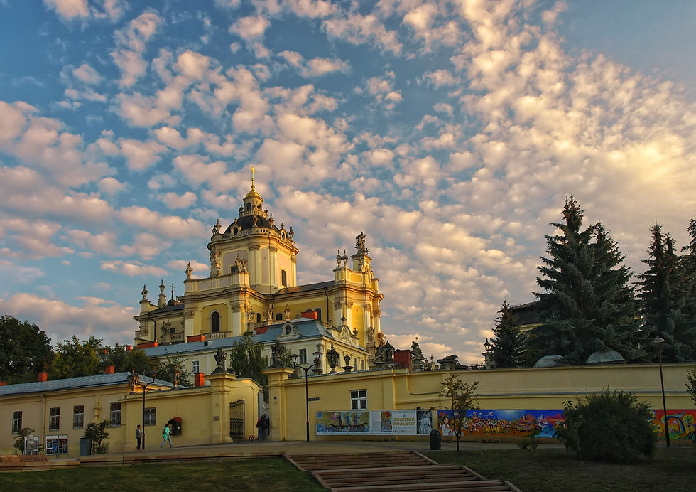 Baroque-style building under a sky with scattered clouds. Trees and a colorful mural adorn the foreground, creating a serene atmosphere.