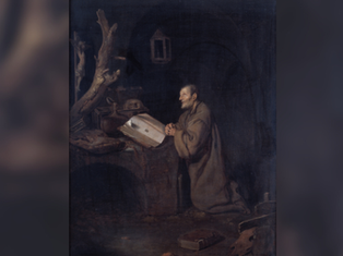 A monk kneels, praying at a desk with an open book in a dark, rustic room. A tree branch and animal skull create a somber mood.