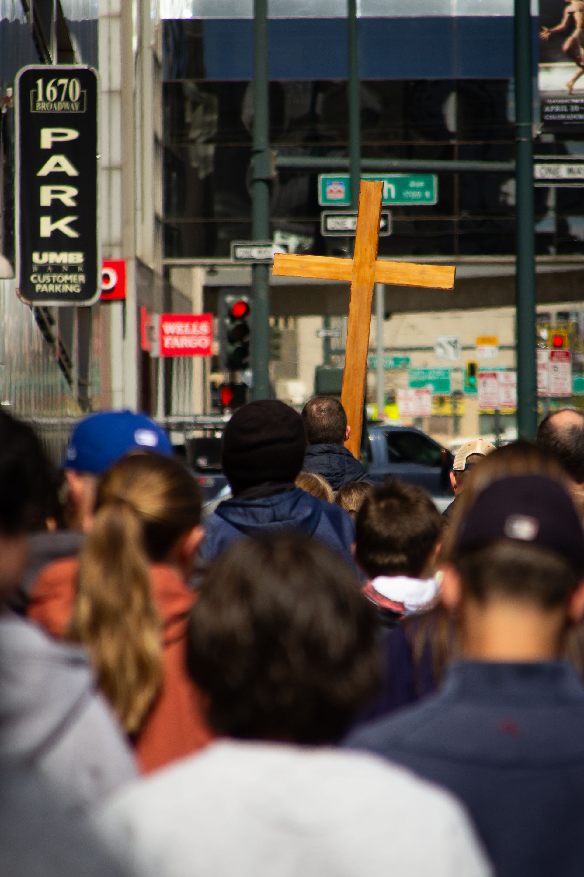 A wooden cross is carried through a busy downtown street as a crowd follows behind in prayer.