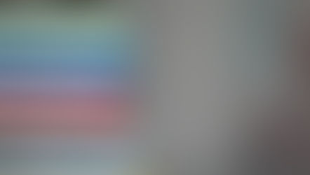 Stack of colorful books with green, blue, red, and yellow spines, against a soft, blurred gray background.