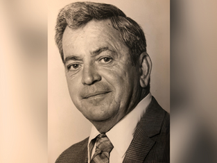 Portrait of a man in a suit and tie, with short hair, smiling slightly against a plain background. Black and white, vintage feel.