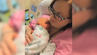 Mother in glasses cradling newborn wrapped in a patterned blanket. Hospital setting. Pink and white tones, tender and calm mood.