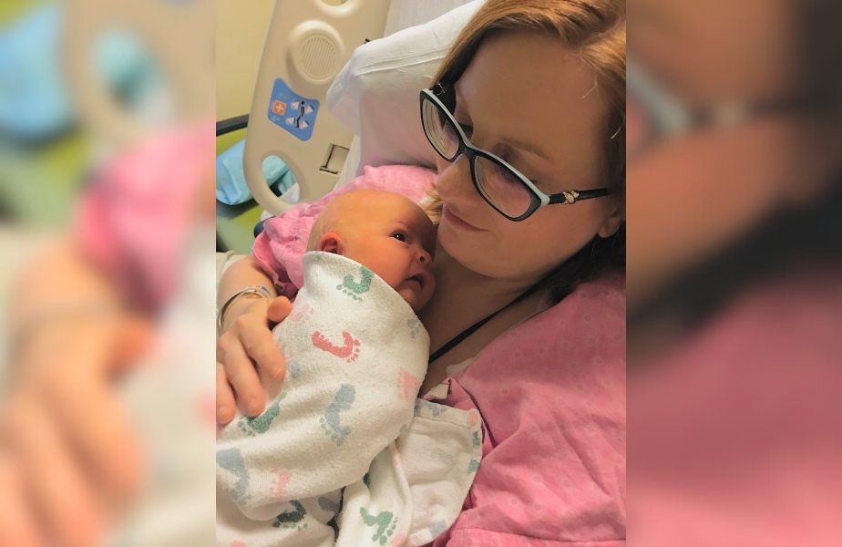 Mother in glasses cradling newborn wrapped in a patterned blanket. Hospital setting. Pink and white tones, tender and calm mood.