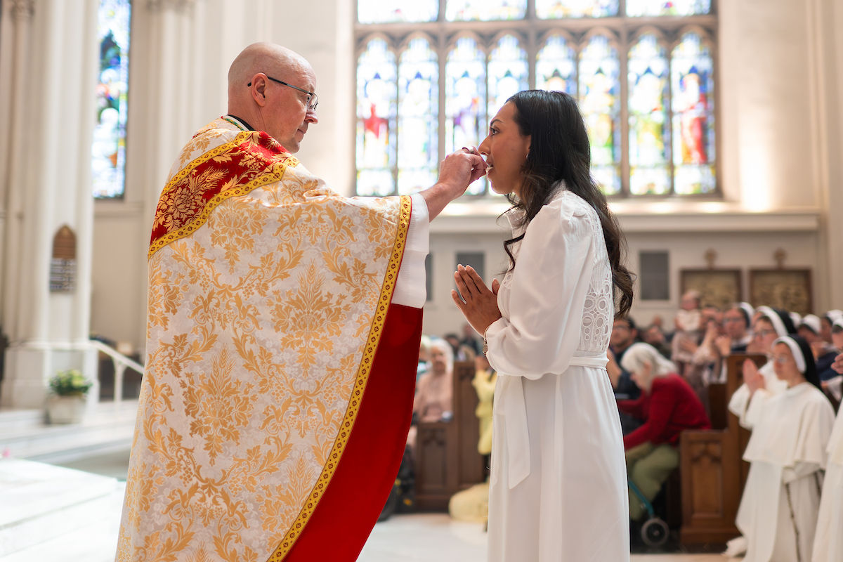 A bishop distributes Holy Communion to a woman with hands folded in prayer.