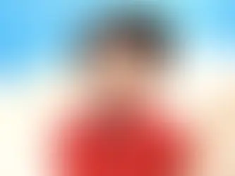 Lego figure with black hair, red shirt, smiling against a blue sky and white cloud backdrop. Playful and cheerful atmosphere.