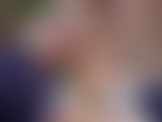 A man prays outdoors, eyes closed, holding rosary beads. Others sit blurred in the background. The mood is calm and reflective.