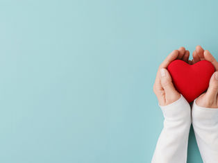 Hands in white sleeves hold a red heart against a pale blue background, conveying warmth and care.
