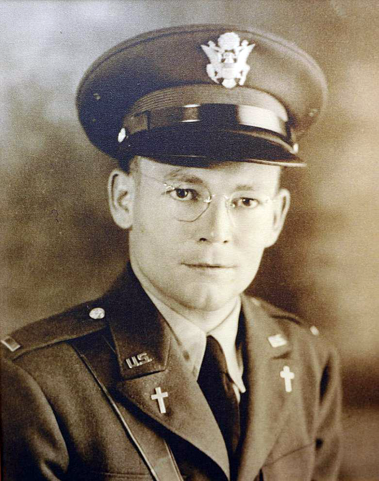 Sepia portrait of a solemn U.S. Army officer in uniform and cap, wearing glasses and religious cross pins.