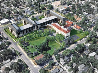 Aerial view of a large complex with modern and historic buildings surrounded by trees in a suburban neighborhood. Roads and houses visible nearby.