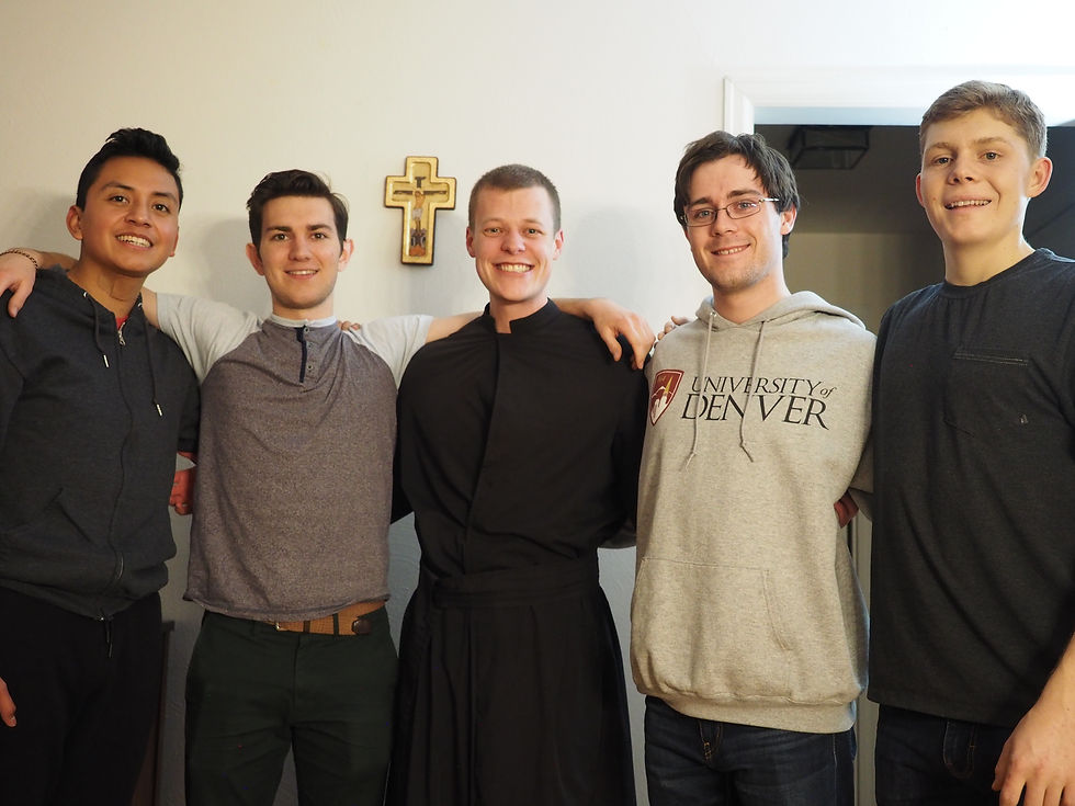 Five young men smiling and standing shoulder to shoulder indoors. One wears a University of Denver hoodie. A cross hangs on the wall behind them.