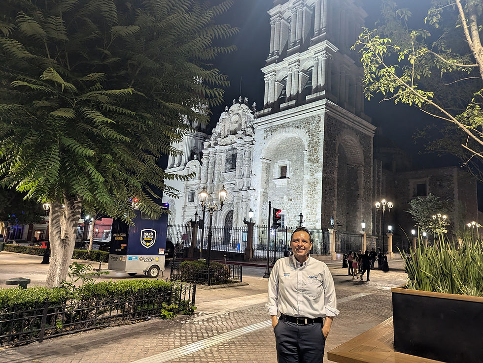 Man smiling in front of an illuminated historic cathedral at night. Trees and a police booth are nearby. The mood is calm and inviting.