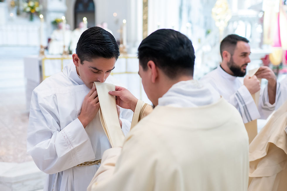 A newly ordained deacon kisses his stole as he is vested for the first time. Soft lighting and altar in the blurred background.