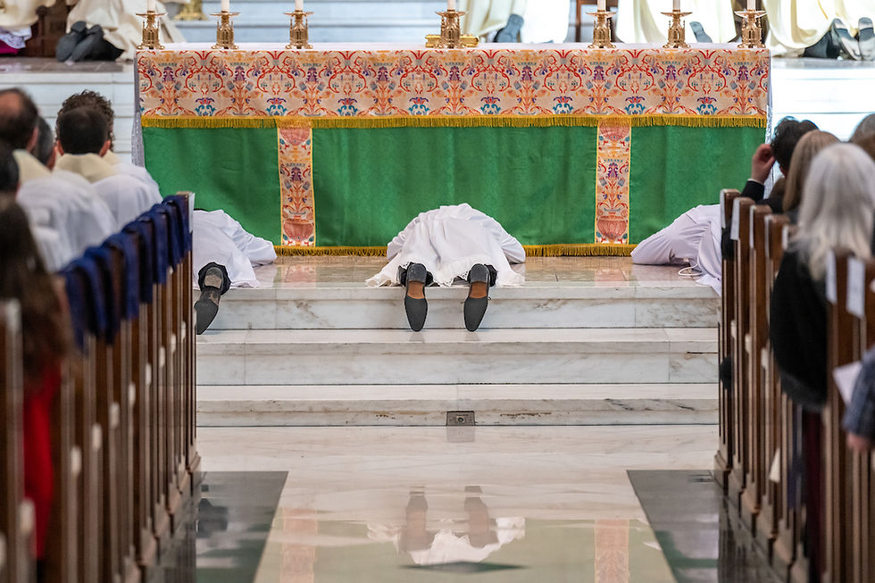 People in white robes lie prostrate before a decorated altar in a church, surrounded by seated onlookers. The atmosphere is solemn.