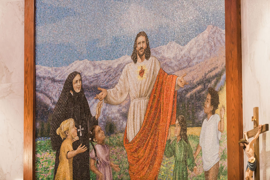 Mosaic mural of Jesus welcoming a nun and children before snowy mountains, with a crucifix at right, in a serene church interior.