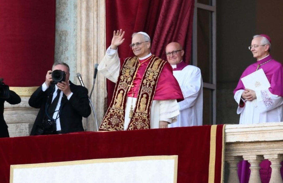 A man in ornate religious attire waves from a balcony, flanked by clerics in white and purple. A photographer captures the moment.