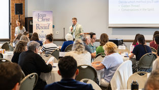 Man speaks into a microphone at a church workshop while seated attendees listen; slide reads Select a scribe and Golden Thread.