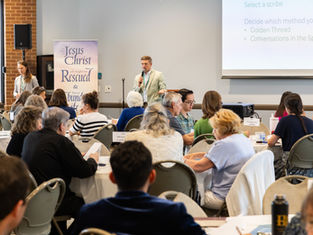 Man speaks into a microphone at a church workshop while seated attendees listen; slide reads Select a scribe and Golden Thread.
