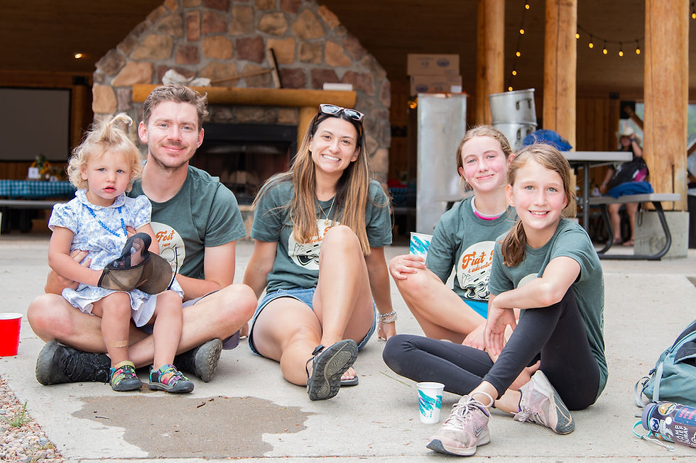 A group of five people, including a child, sitting on a patio in front of a stone fireplace, smiling. They're wearing matching green T-shirts.