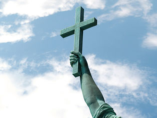 Bronze statue arm holding a cross aloft against a blue sky with scattered clouds