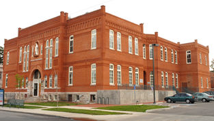 Red brick building with white-trimmed windows, featuring a statue above the entrance. Cars parked in front. Cloudy sky. Calm setting.