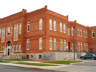 Red brick building with white-trimmed windows, featuring a statue above the entrance. Cars parked in front. Cloudy sky. Calm setting.