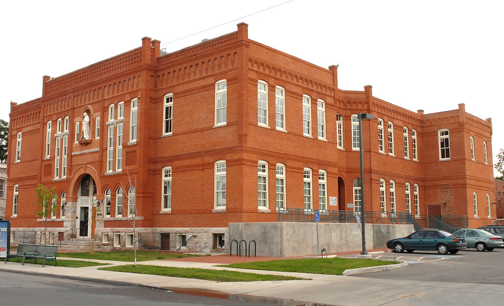 Red brick building with white-trimmed windows, featuring a statue above the entrance. Cars parked in front. Cloudy sky. Calm setting.