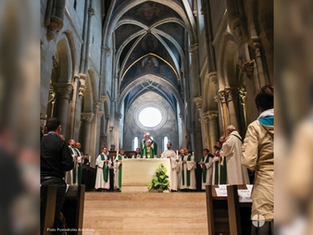 Clergy conduct a service in a grand cathedral with high arches, wearing white and green robes. Attendees watch solemnly in the foreground.