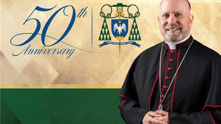 A smiling cleric in black robes. "50th Anniversary" text and a crest appear on a beige and green background.