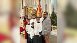 A family dressed in church robes poses inside a cathedral surrounded by poinsettias and a Christmas tree, exuding joy and warmth.