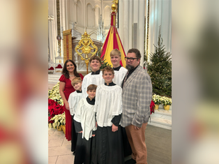 A family dressed in church robes poses inside a cathedral surrounded by poinsettias and a Christmas tree, exuding joy and warmth.