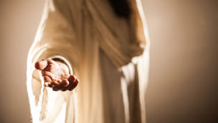Outstretched hand in a flowing, cream-colored robe, reaching forward in soft lighting. Background is blurred, creating a serene atmosphere.