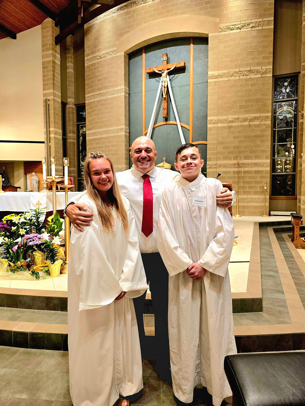 Three people smiling in a church; two in white robes, one in a suit with red tie. A cross is visible in the background.