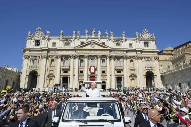 A white-clad figure waves from a vehicle in front of a grand cathedral, greeted by a crowd. Clear blue sky and vibrant atmosphere.