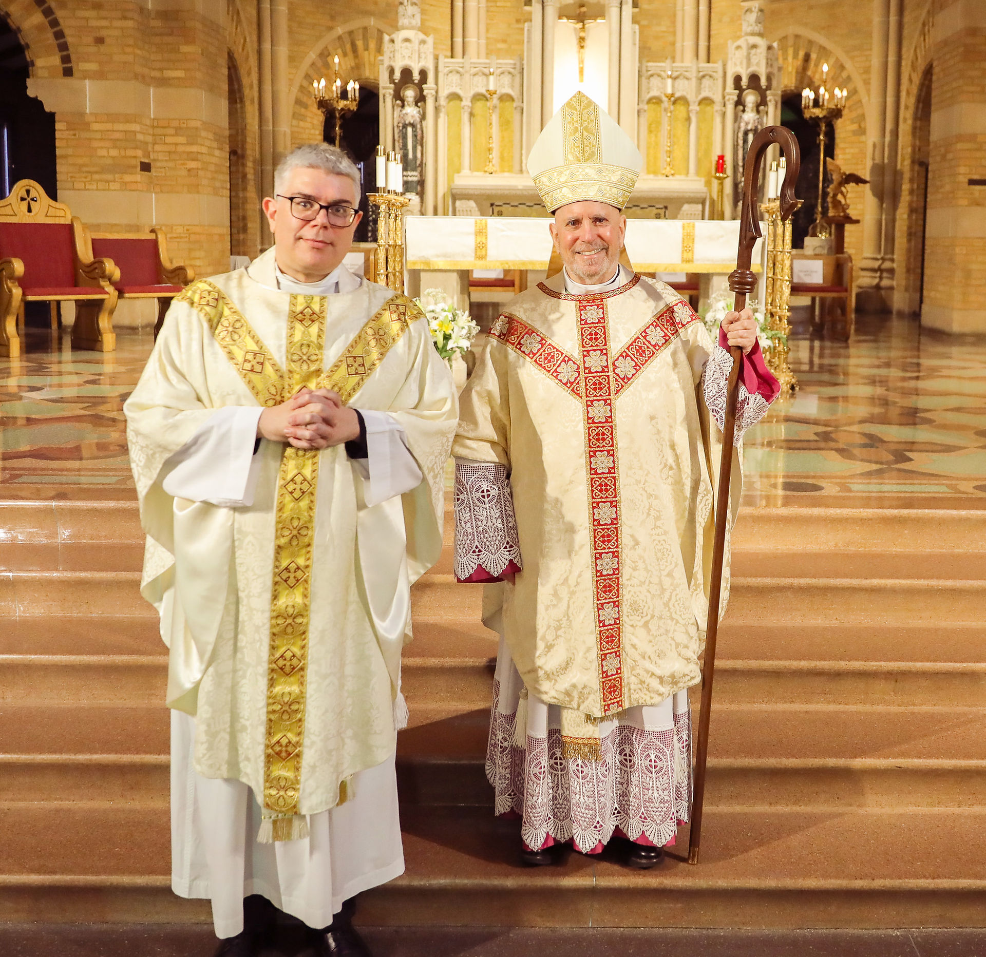A priest and an archbishop stand in an ornate chapel after a religious ceremony.