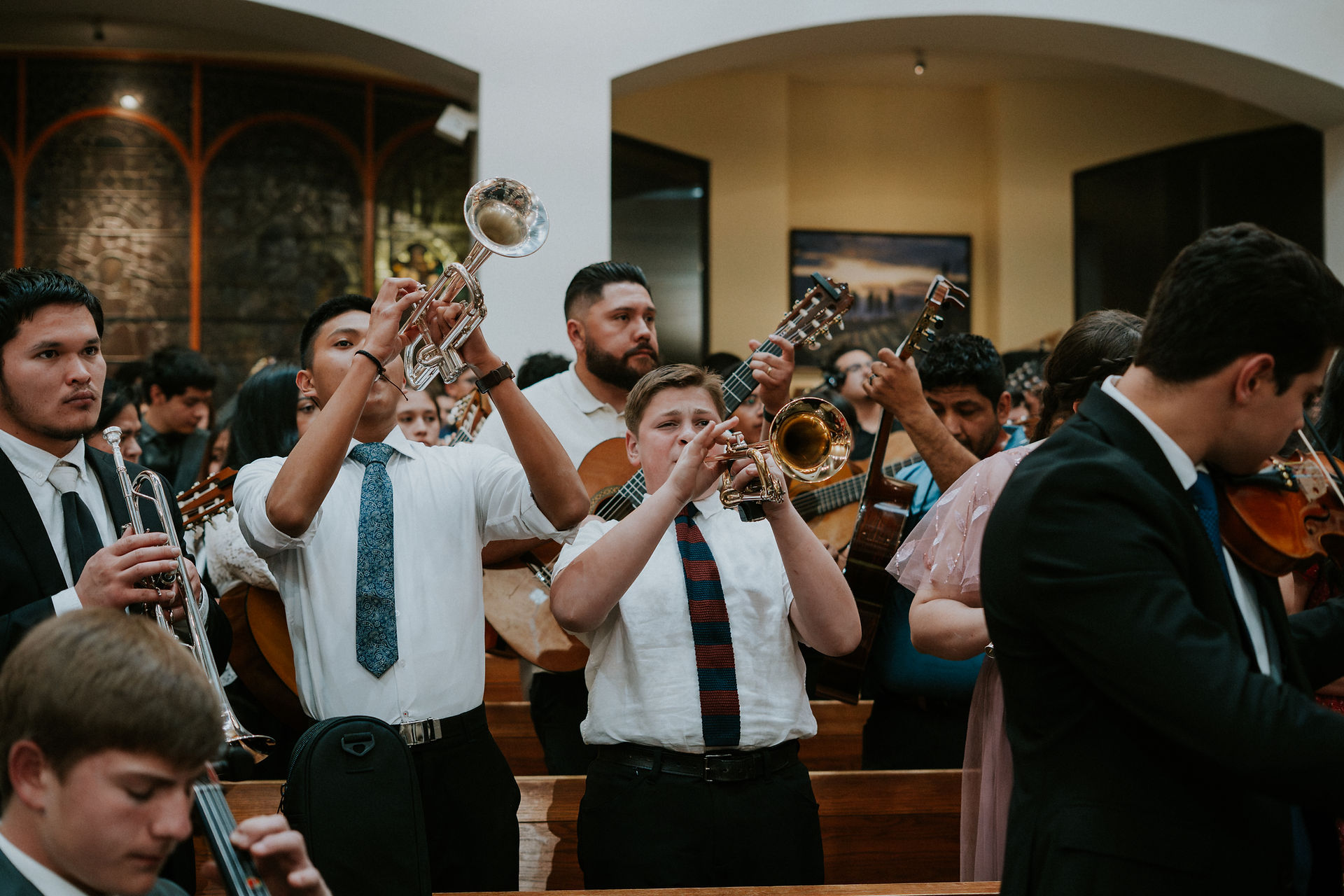 A group of musicians in formal attire play trumpets, guitars, and violins in a church setting, creating a lively and focused atmosphere.