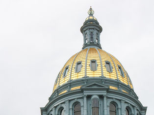 Gold-domed capitol building against a cloudy sky. Detailed architecture with arches and windows. Calm and majestic setting.