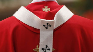 Close-up of a red-and-white religious vestment with gold and black cross embroidery against a blurred background