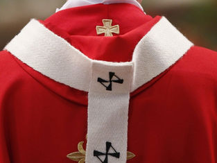 Close-up of a red-and-white religious vestment with gold and black cross embroidery against a blurred background
