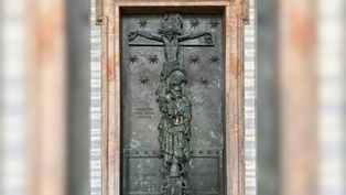 Bronze relief on a door showing a figure on a cross with stars. Text reads "CHRISTUS HER MUNDI" and dates "A.D. 2000." Stone frame.