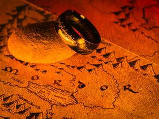 A golden ring with inscriptions lies on a rock atop a sepia-toned map of Mordor, in warm, dramatic lighting.