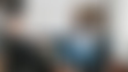 Two women in therapy session; one on chair taking notes, the other on a couch talking, smiling. Neutral-toned room with light walls.