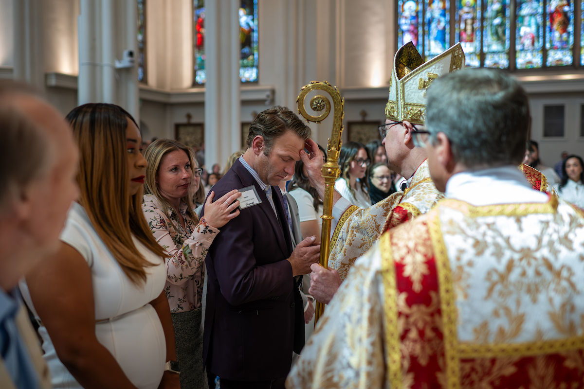 A bishop places his hand on a man’s head in blessing as others stand nearby.