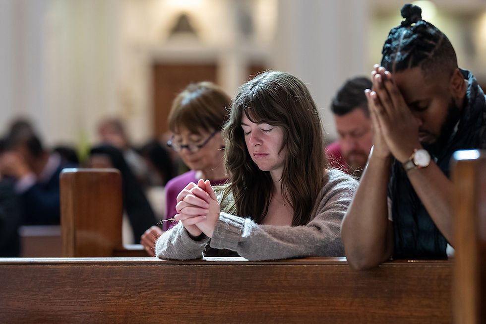 People praying in a church, eyes closed, hands clasped. Wooden pews and soft lighting create a serene atmosphere.