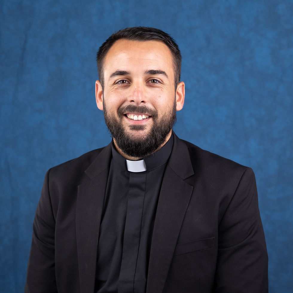 Smiling bearded priest in black clerical suit with white collar against a blue studio backdrop