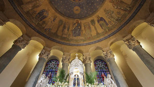 Ornate church interior with murals of biblical figures, stained glass windows, and a central altar adorned with lilies, evoking a serene mood.
