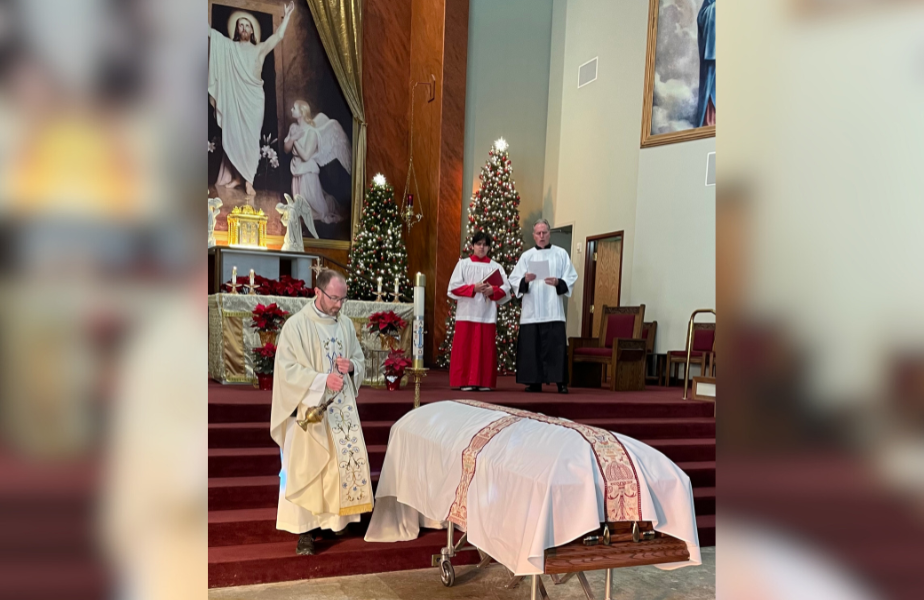 A priest conducts a funeral service in a church, standing beside a casket. Altar servers stand behind. Christmas trees and religious art decorate the background.