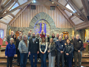 Group of people smiling in a church with wooden beams and stone walls. A crucifix is in the background, creating a warm and inviting atmosphere.
