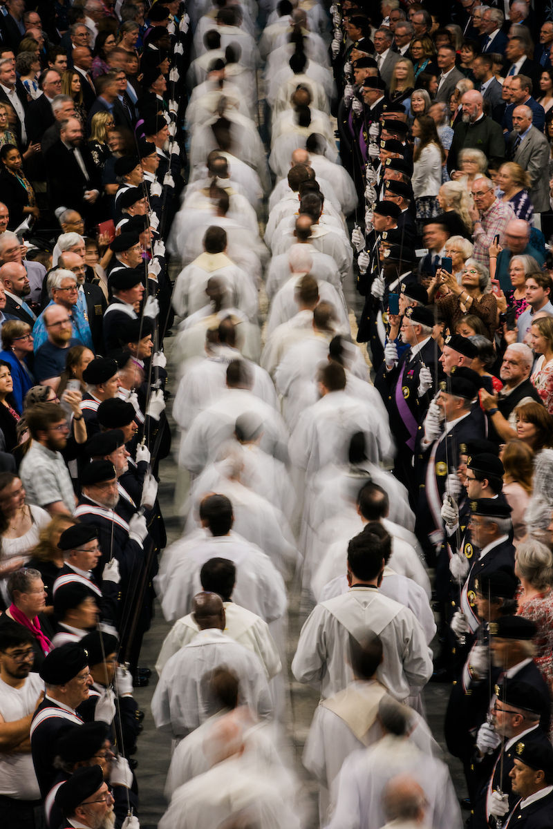 Priests process between rows of attendees and honor guards during the liturgical entrance.